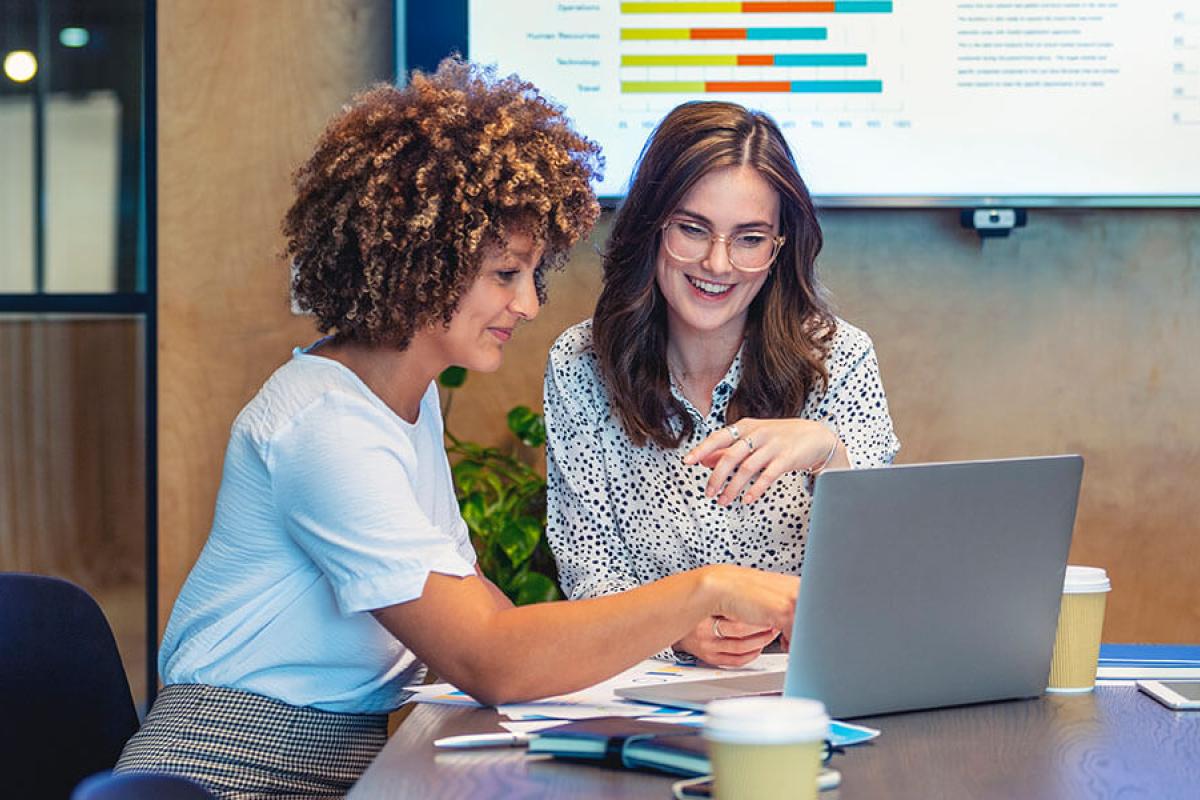 Two professionals work together on a laptop in a boardroom.