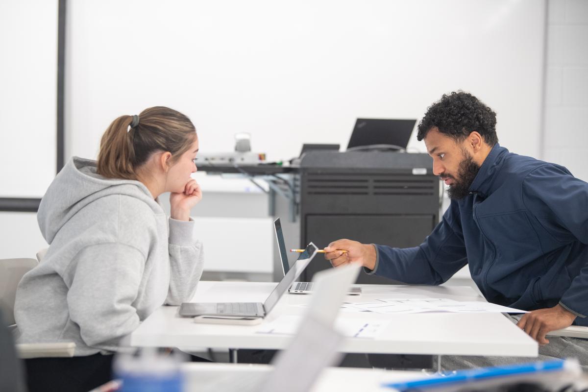 Two economics students working together with laptops and printer in the background.