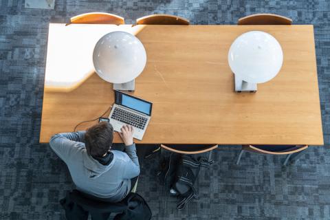 Campus library table with two lamps and student working on a laptop.