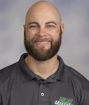 Alum Jake Suval. He is wearing a gray polo shirt and is posed in front of a professional, gray background.