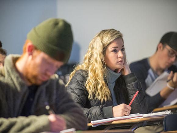 Students take notes while sitting in a classroom.