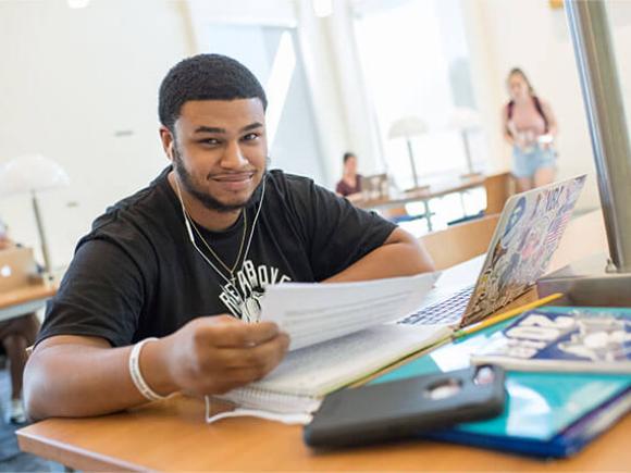 A Westfield University student works on their homework at a table in a common area.