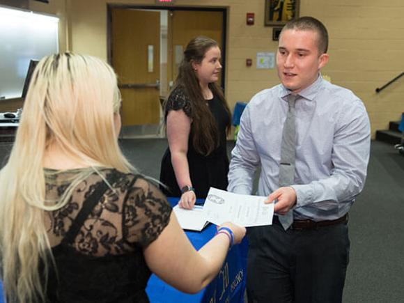 A student being handed a certificate in a classroom setting.