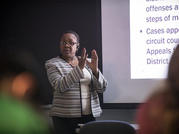 A Criminal Justice professor stands in front of a projection screen while instructing their class of students.