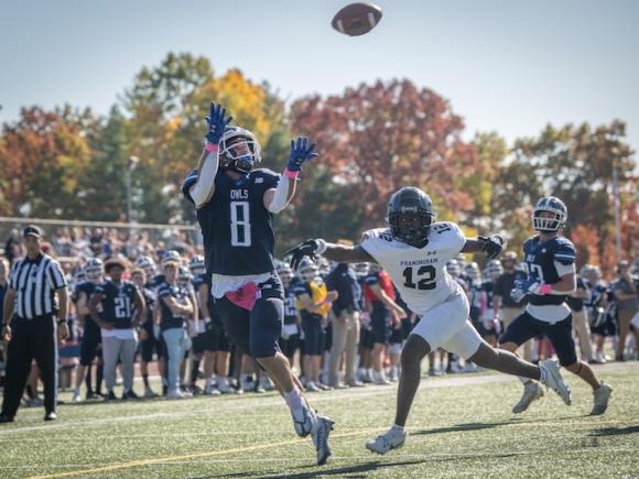 The Westfield State Owls football team against Fitchburg State. A receiver jumps into the air to catch a pass, with a player from Fitchburg close behind him.