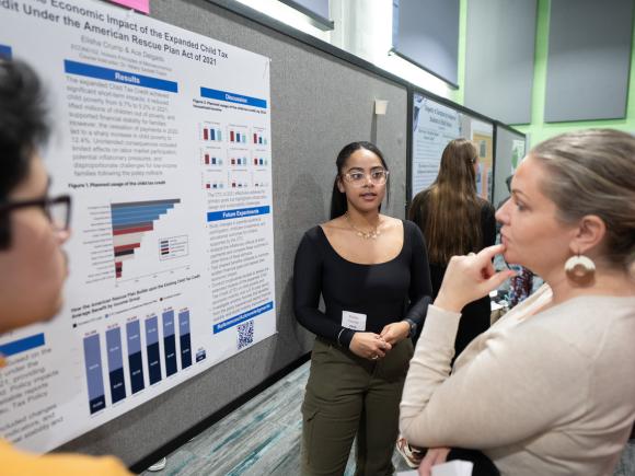 Student at undergraduate research event presenting their research poster to a faculty member.