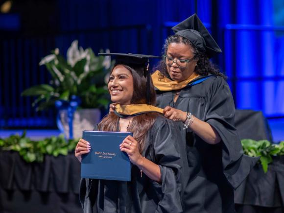 Female places academic hood on graduate