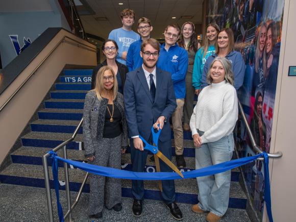 Students, staff and university president stand at ribbon cutting for ely center