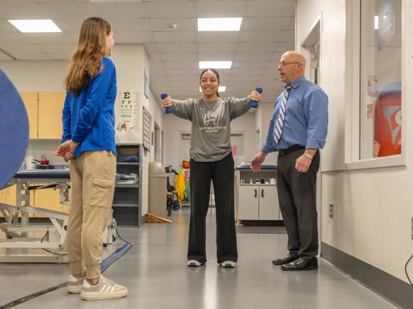 Student holding weights during an athletic training class while working with a faculty member.