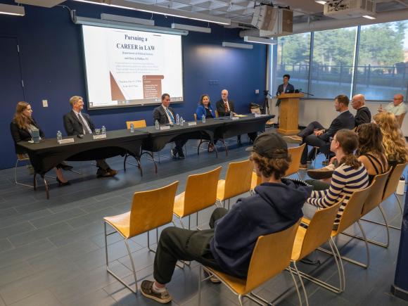 Legal professionals participate in Westfield State University's Pursuing a Career in Law forum as students listen from the audience and a moderator stands at the podium
