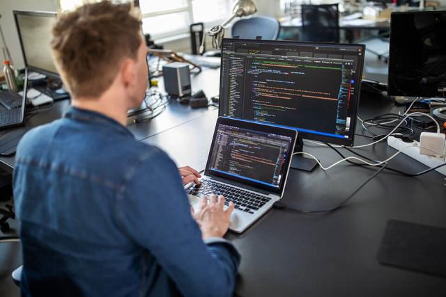 A person works on a laptop set in front of an additional monitor.