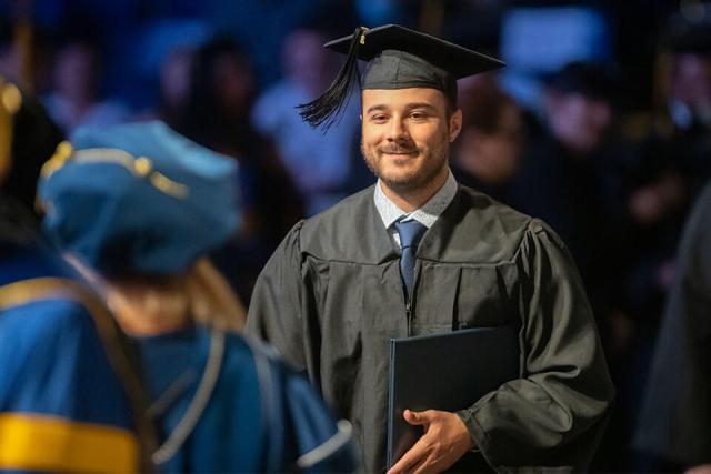 A student wearing a cap and gown holds their diploma at their graduation ceremony.