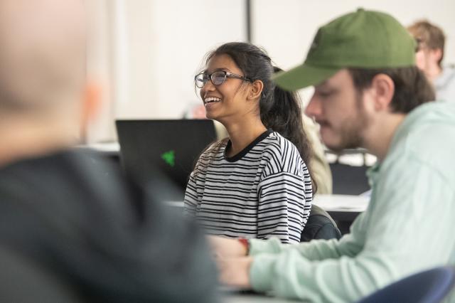 CIS student wearing black and white striped shirt with glasses and pony tail smiling in classroom.