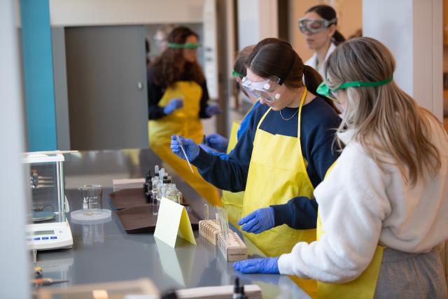 Students in chemistry classroom wearing lab aprons and eye protection.