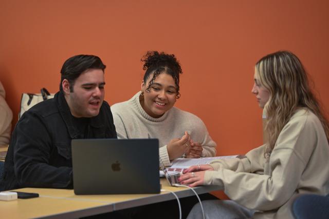 Three students working on a classroom project together looking at a laptop.