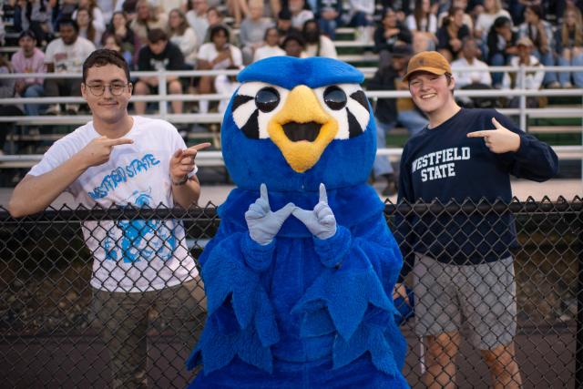 Nestor the mascot smiling with two students at a football game.