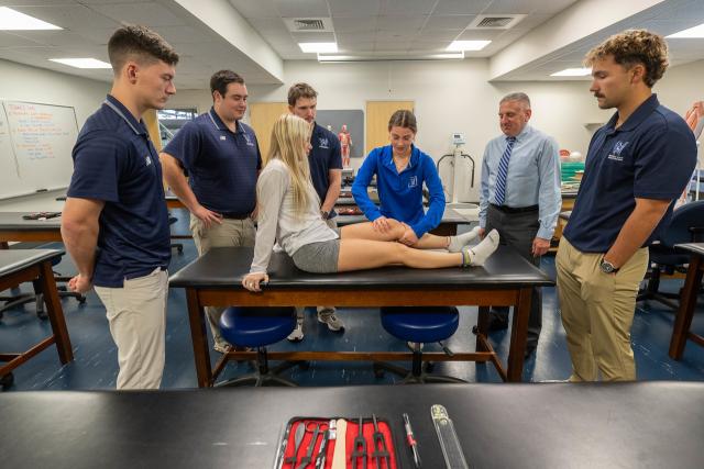 Students and faculty in an athletic training class practicing how to stabilize a knee.