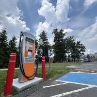 The electric vehicle charger in the Commuter Lot. It is an orange machine and flanked by two, red safety pillars.