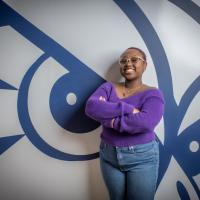 Catrina Casting, class of 2026. She is posing in front of a navy blue and white owl, and wears a purple shirt and jeans.