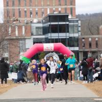 Girls on the Run, hosted on November 24. A crowd of people run towards the camera in front of the Ely Campus Center for the 5K event.